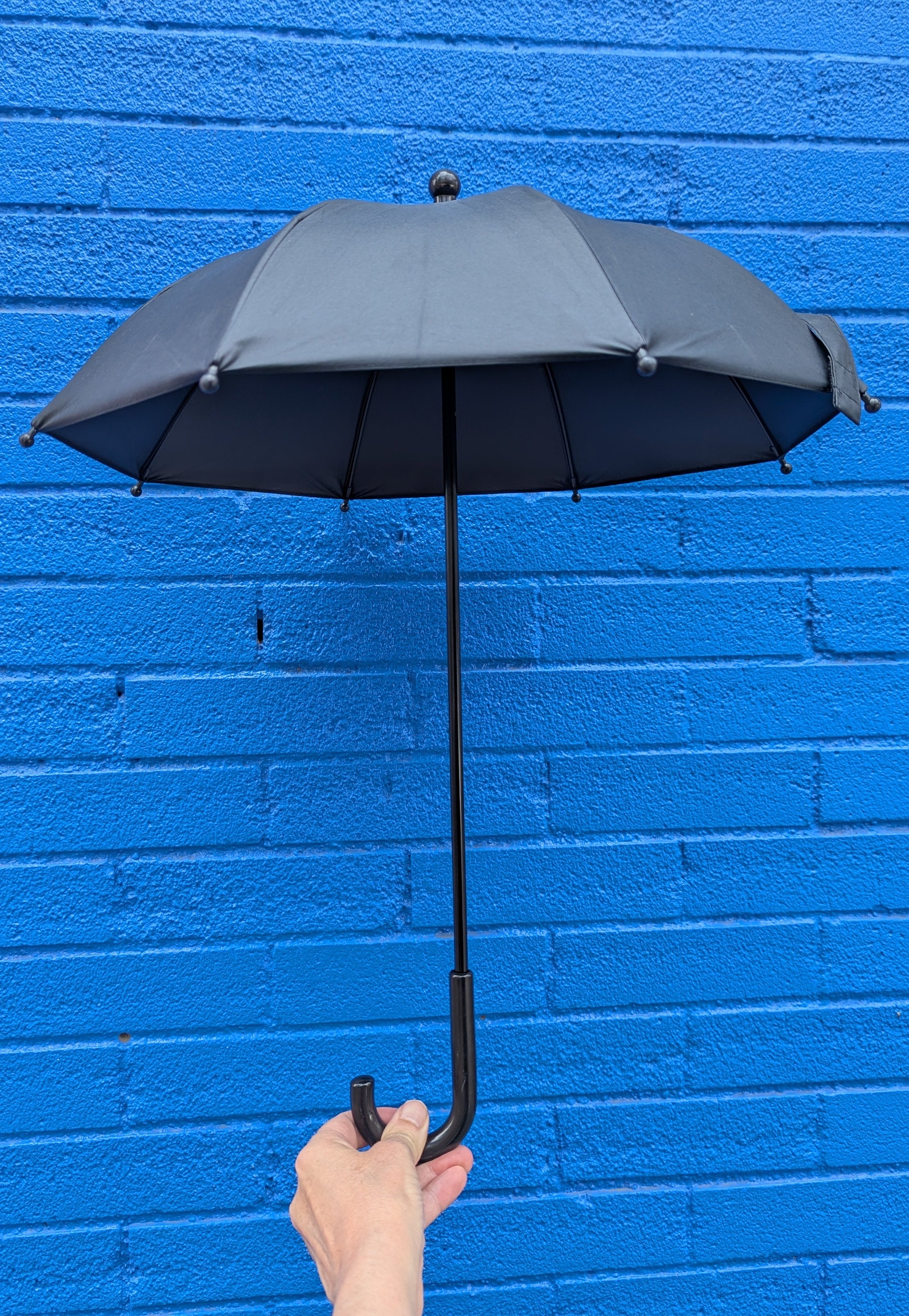Hand holding a black parasol against a blue brick wall