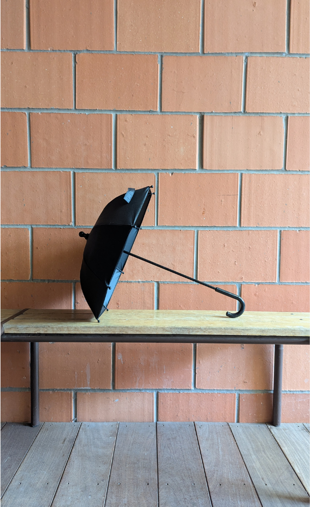 Black umbrella on a wooden bench against a brick wall